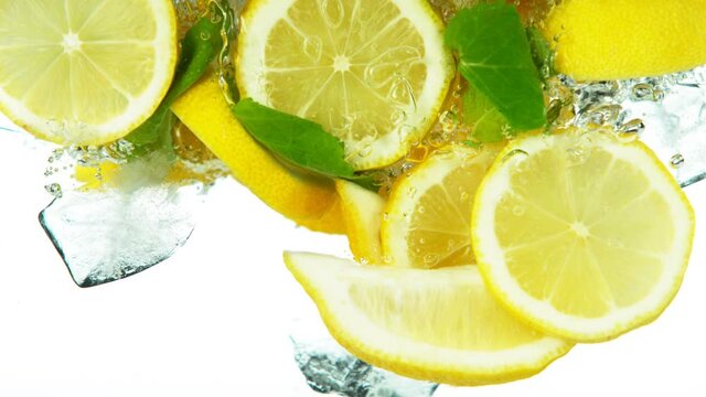 Super slow motion of lemon slices falling into water with ice cubes on white. Filmed on high speed cinema camera, 1000 fps.