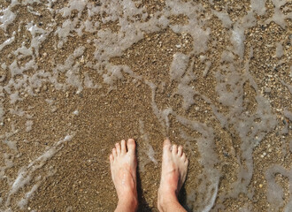 Legs of a barefoot man in the foamy sea with sand close-up. Rest and vacation. Photography, concept, top view.