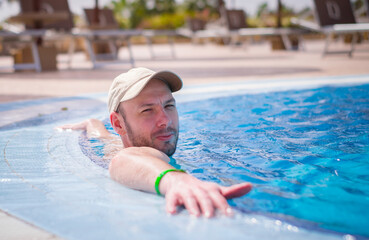 A man in a cap is resting in the pool. Portrait of a guy in the pool of an expensive hotel.