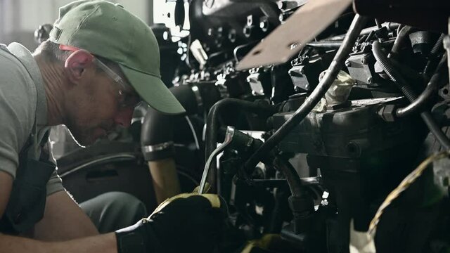 Caucasian Male Repairman Servicing Coach Bus Engine By Adjusting Bolts With Wrench. 