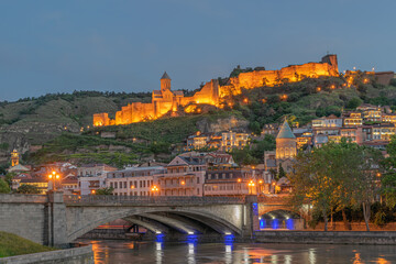 Cityscape of illuminated historic old Tbilisi with ancient Narikala fortress, Sioni Cathedral,  Metechi stone Bridge over the Mtkvari/Kura river and  mosque in the evening. Tbilisi, Georgia © levan