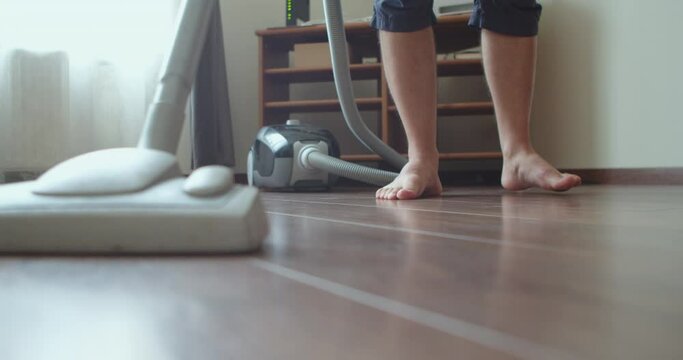 Young man doing housework with a vacuum cleaner in his hand. A man vacuums in a bright room early in the morning at the weekend.