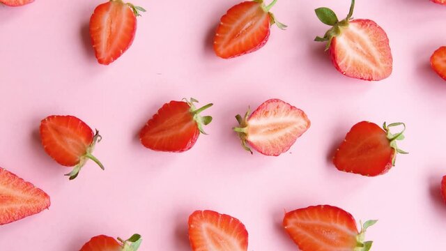 Pink rotating background with juicy strawberry halves, top view