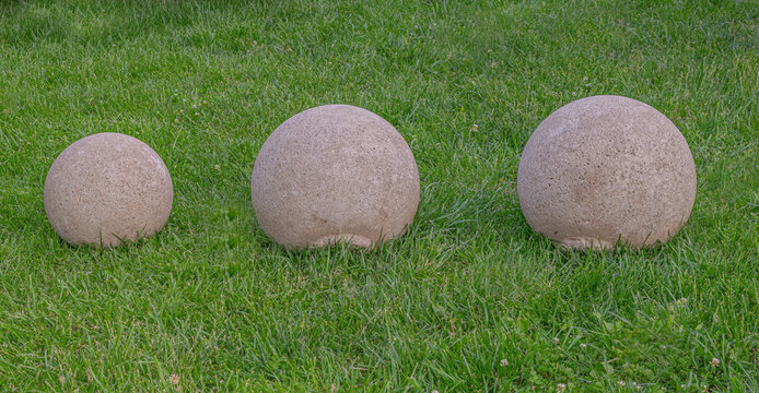 Close-up view of different size three decorative spherical concrete globes/balls in the green grass. Tbilisi Georgia 