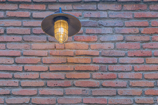Close-up of nautical style outdoor metal lantern illuminating red brick wall in the evening. Tbilisi, Georgia
 