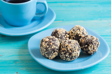 Five homemade energy balls on a plate and a Cup of coffee on a blue wooden table. Healthy homemade chocolate dessert for Breakfast will fill you with energy