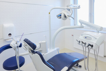A modern interior of a dental office with white and blue furniture, dental chair, drills. Dentist’s office.