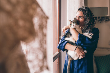 Adult woman indoor holding cat - Woman at home standing window hugging kitten