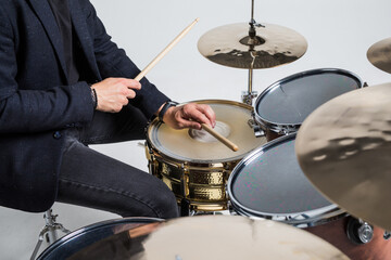 Close up of hands of male drummer holdning drumsticks sitting and playing drums on white background