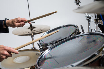 Close up of hands of male drummer holdning drumsticks sitting and playing drums on white background
