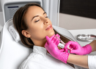 Woman with beautiful clean skin. Cosmetologist does injections for lips augmentation and anti...