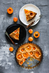 Apricot pie, a white and a black plate with pieces of a pie and forks, apricots around. Grey background, top view
