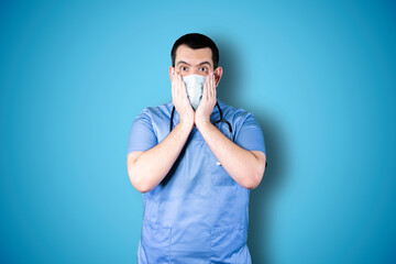 Doctor with mask over isolated blue background studio with surprise facial expression