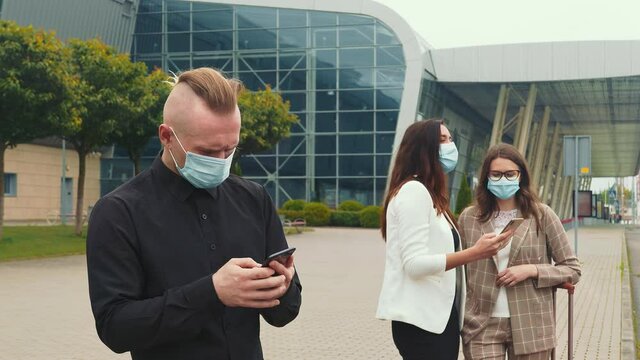 A male businessman and two girls in medical masks with a mobile phone browse the contents of the phone and laugh emotionally. Emotions of girls while watching a mobile phone.