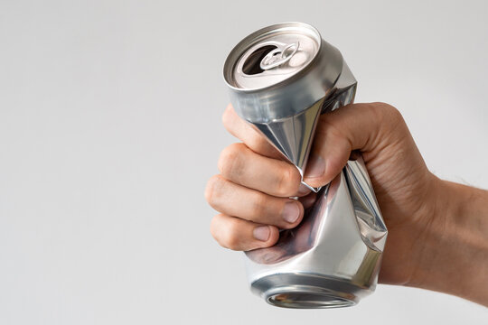 male hand squeezes an empty aluminum can for recycling