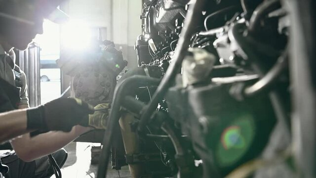 Caucasian Male Car Mechanic Inspecting And Repairing Bus Engine In Automotive Garage. 
