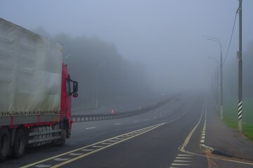 Early morning driving truck on highway in fog. Autumn, dry weather, foggy grey sky. One truck on the road. Lonely vehicle on the motorway.