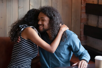 African ethnicity millennial couple in love hugging while sit in cafe during romantic date. Female...