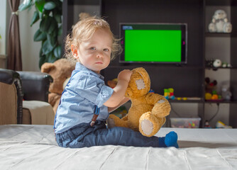 Cute baby boy and his teddy bear watching TV sitting on a couch in the living room at home