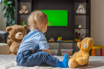 Cute baby boy and his teddy bear watching TV sitting on a couch in the living room at home