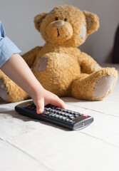 Baby hand holding the TV remote control, teddy bear in the background, selective focus