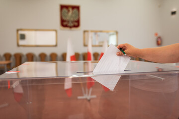 Throwing a card with a vote.to the ballot box during  elections. In the backround polish emblem and...