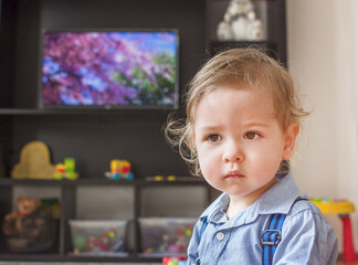 Cute baby boy sitting on the floor in front of the TV, at home
