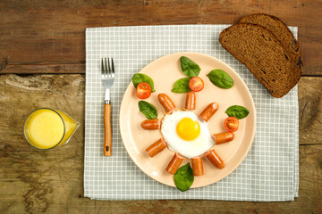 Scrambled eggs with sausages in the shape of a sun. Children's breakfast with bread on a napkin and a glass of juice.
