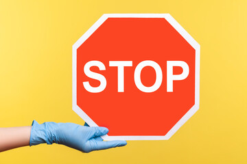 Profile side view closeup of human hand in blue surgical gloves holding and showing Stop sign....