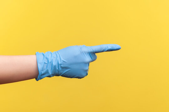 Profile side view closeup of human hand in blue surgical gloves showing or pointing ot something with finger. indoor, studio shot, isolated on yellow background.