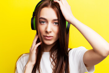 Beautiful young girl model listens to music in headphones on a yellow background