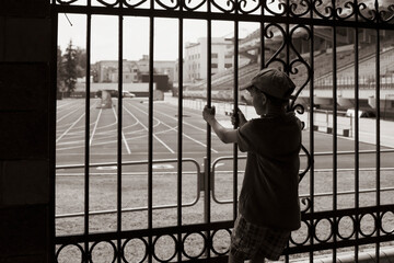 A small boy looks at the stadium through the fence