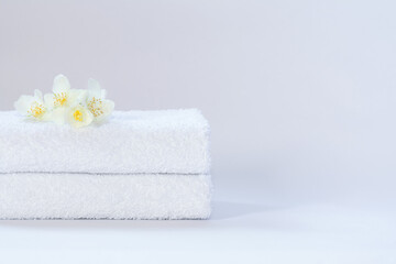 Obraz na płótnie Canvas Two white neatly folded terry towels with a jasmine flower on a light background.