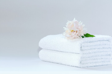 Two white neatly folded terry towels with a delicately pink peony flower on a light background.