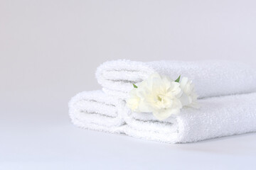 Fototapeta na wymiar Three white neatly folded terry towels with a jasmine flower on a light background.