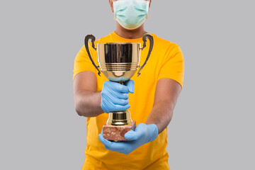 Fototapeta na wymiar Indian Man Holding Trophy in Hands Wearing Medical Mask and Gloves Close Up Isolated