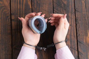 female hands in handcuffs hold twisted money on a dark wooden background