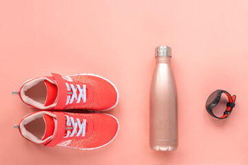 Red sneakers, sport watch and bottle with water on coral pink background. Concept of healthy life, top view, flat lay, copy space