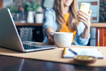 Business woman having a facetime video call. Happy and smiling girl working from home office kithcen and drinking coffee. Using computer and mobile phone. Distance learning online education and work