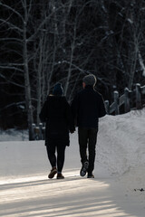 Fototapeta na wymiar Young couple walking along a snowy pathway on a date. People walking in the park during winter. Walking away on a path in the snow portrait