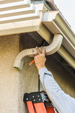 Worker Attaching Aluminum Rain Gutter And Down Spout To Fascia Of House