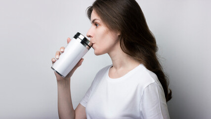 Girl in a white T-shirt drinks coffee from a thermocup