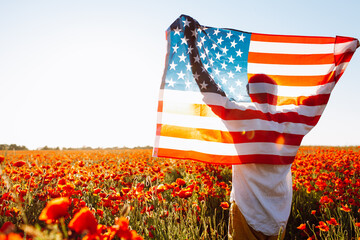 A man with flag of the United States on a shoulder in beautiful poppy field on a clear, sunny day....