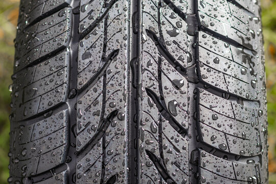 New tire. There are raindrops on it. The tread pattern is looking at us. Close-up.