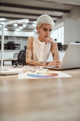 Successful businesswoman. Pretty and young tattooed female designer using laptop while working at...