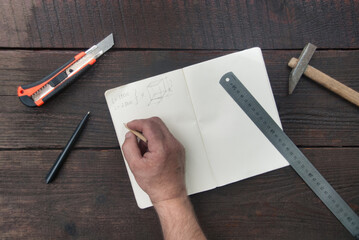 Building, architecture, construction concept. Flat lay of a male hand writting calculations in a notebook with building tools around