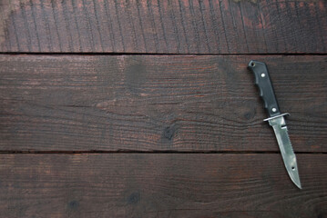Black hunting knife laying on the dark wooden table. Copy space. Flat lay