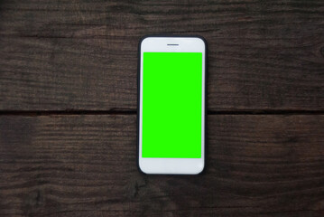 White smartphone with green screen on a dark wooden table. Flat lay. Cellphone on a vintage background. Blank text place