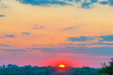 Grassy fields and trees with lush green foliage in green rolling hills below a blue sky in the light of sunset in summer