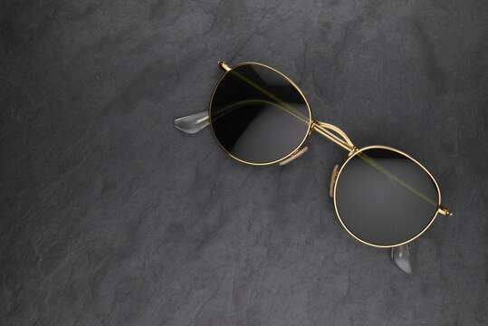 Gold Frame Round Black Sunglasses On Black Slate Background.